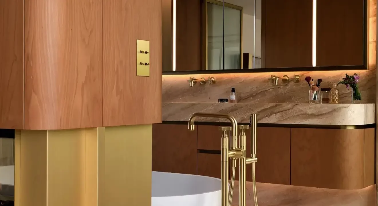 Interrupteur en finition doré chaud dans une salle de bain avec une robinetterie doré et des teintes chaudes en bois et du marbre crème